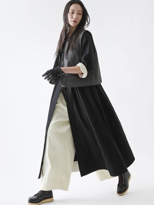 Soh dark grey gilet layered over a long black coat and cream trousers