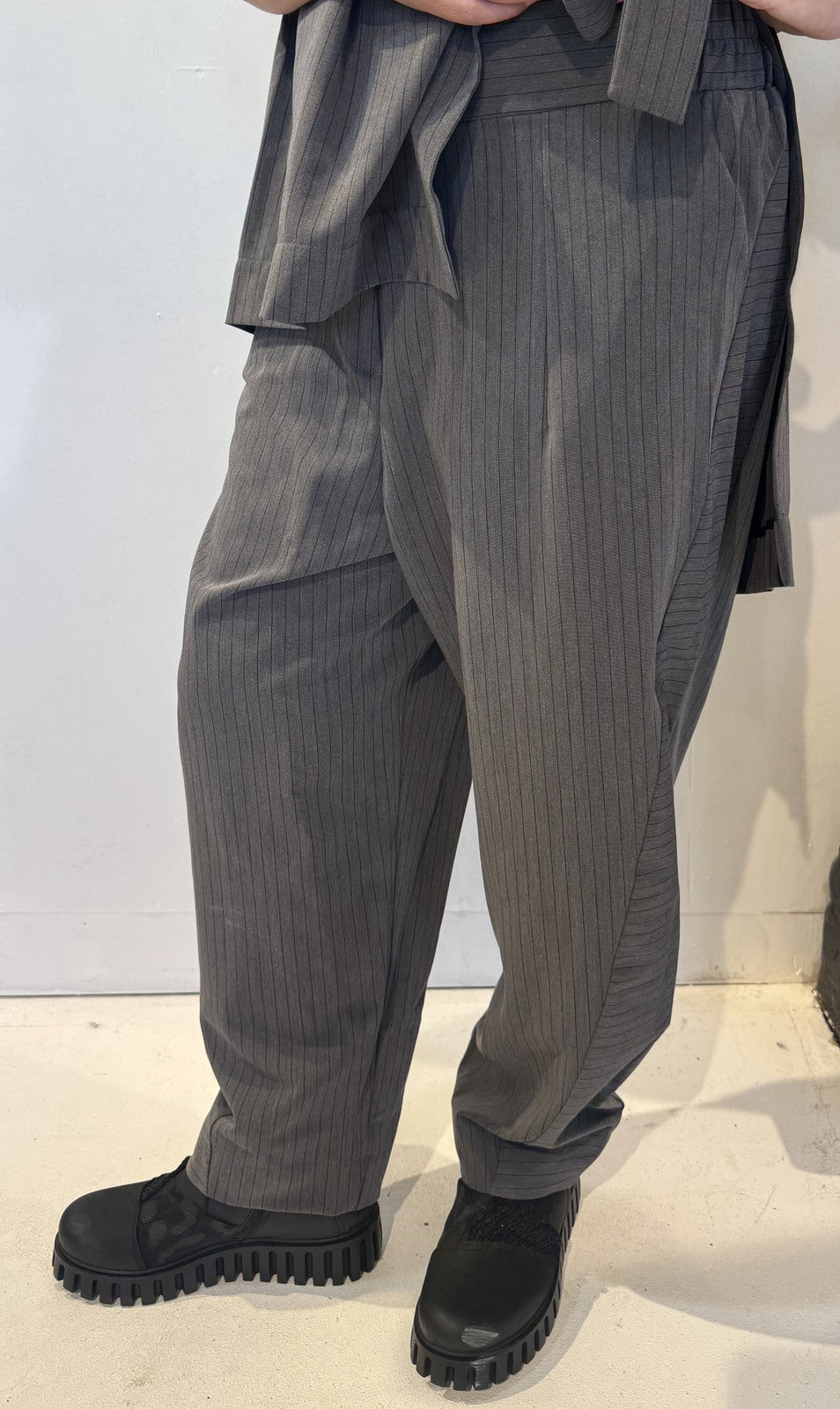 Front view of the Igor Dobranic Calla grey pinstriped trousers showing their rounded legs and broad hem bands
