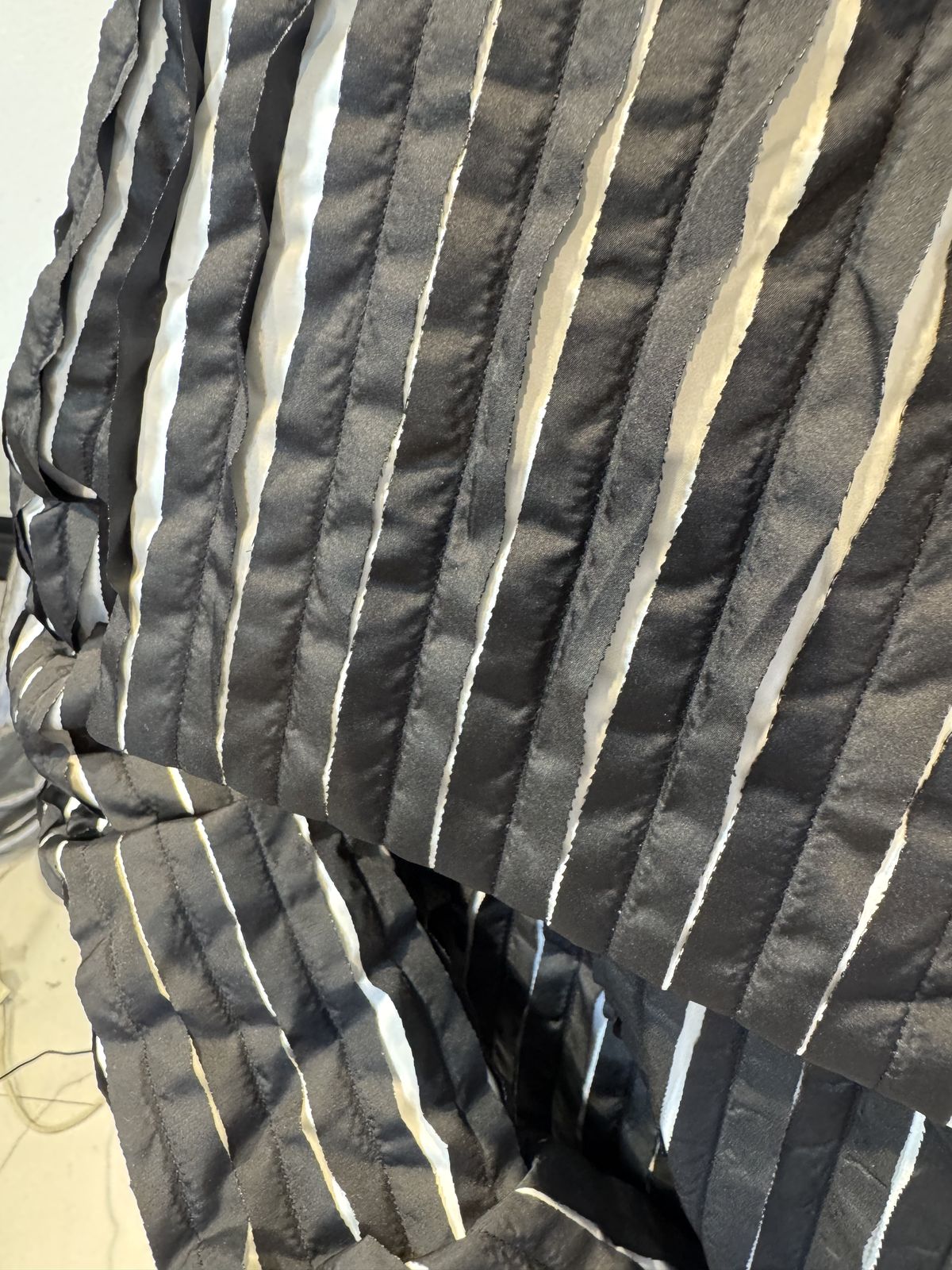 Detail of the Magnolia coat showing rippled black fabric and narrow white stripes