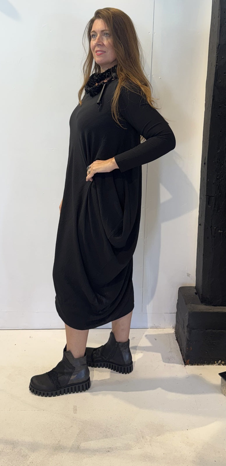 Side view of the Strelizia black dress showing the fabric gathered into soft folds
