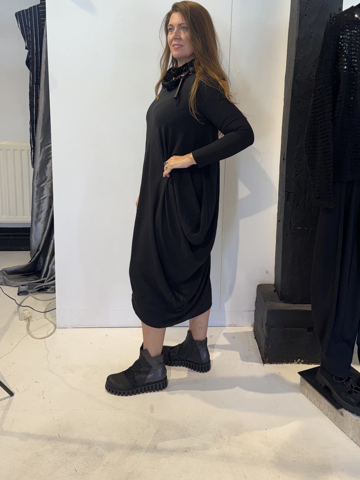 Side view of the Strelizia black dress showing the fabric gathered into soft folds