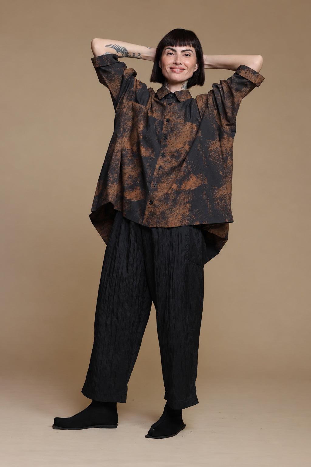 Copper-brown and charcoal shirt, relaxed pose with arms behind the model's head