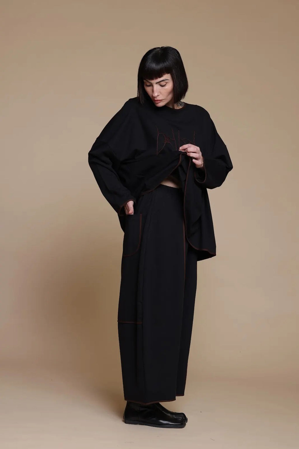Black shoe-artwork top, styling view with the hem lifted at one side